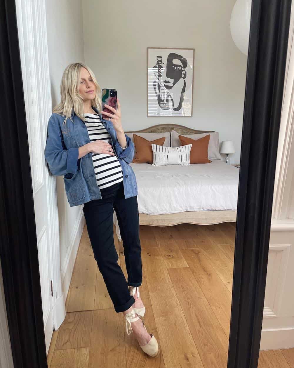 Pregnant woman wearing a denim jacket over a striped t-shirt with black jeans 