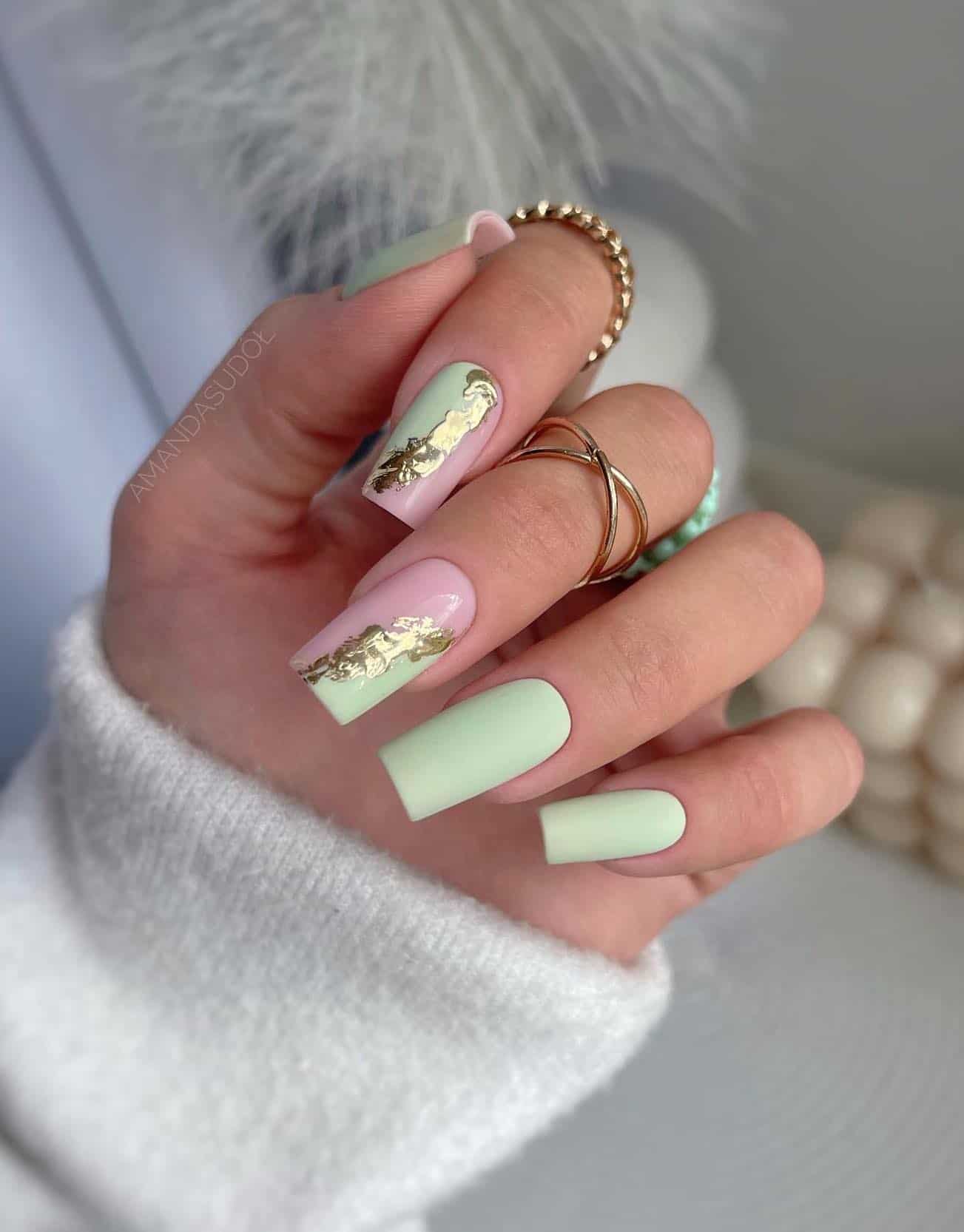 A hand with long square nails painted a matte mint green and two accent nails with matte mint green and glossy pink polish with gold in between