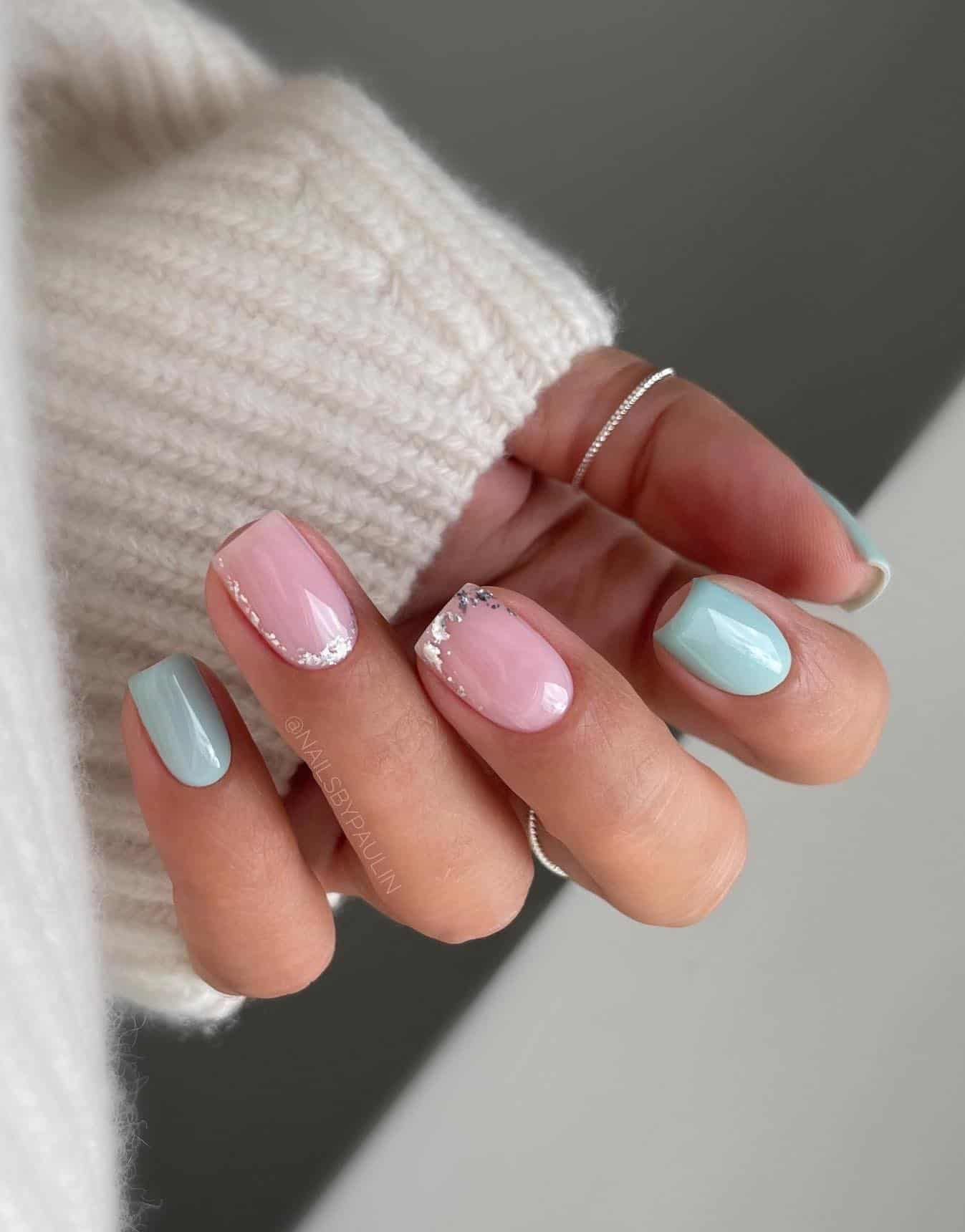 A hand with short square nails painted a soft mint green with two nude pink accent nails with silver flake details