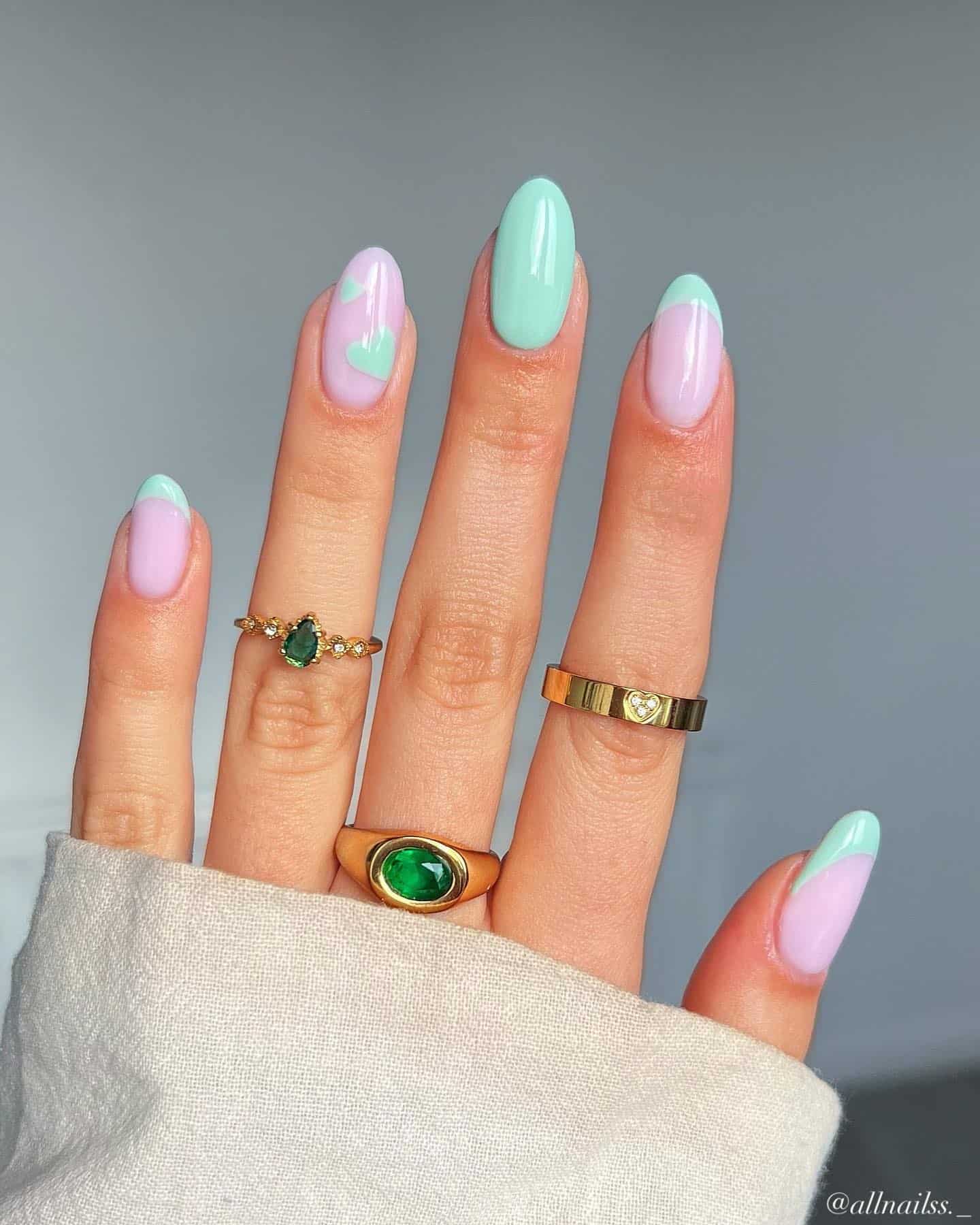 A hand with pink almond nails painted with mint green French tips and two accent nails, one with solid mint green polish and the other with mint green hearts
