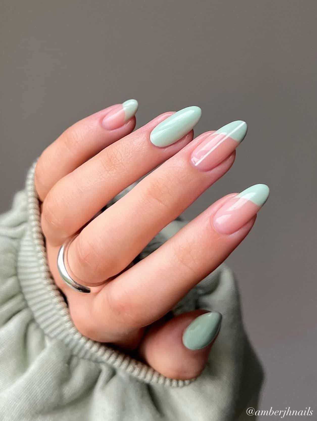 A hand with medium almond nails with asymmetrical mint green French tips and two solid colored mint green nails