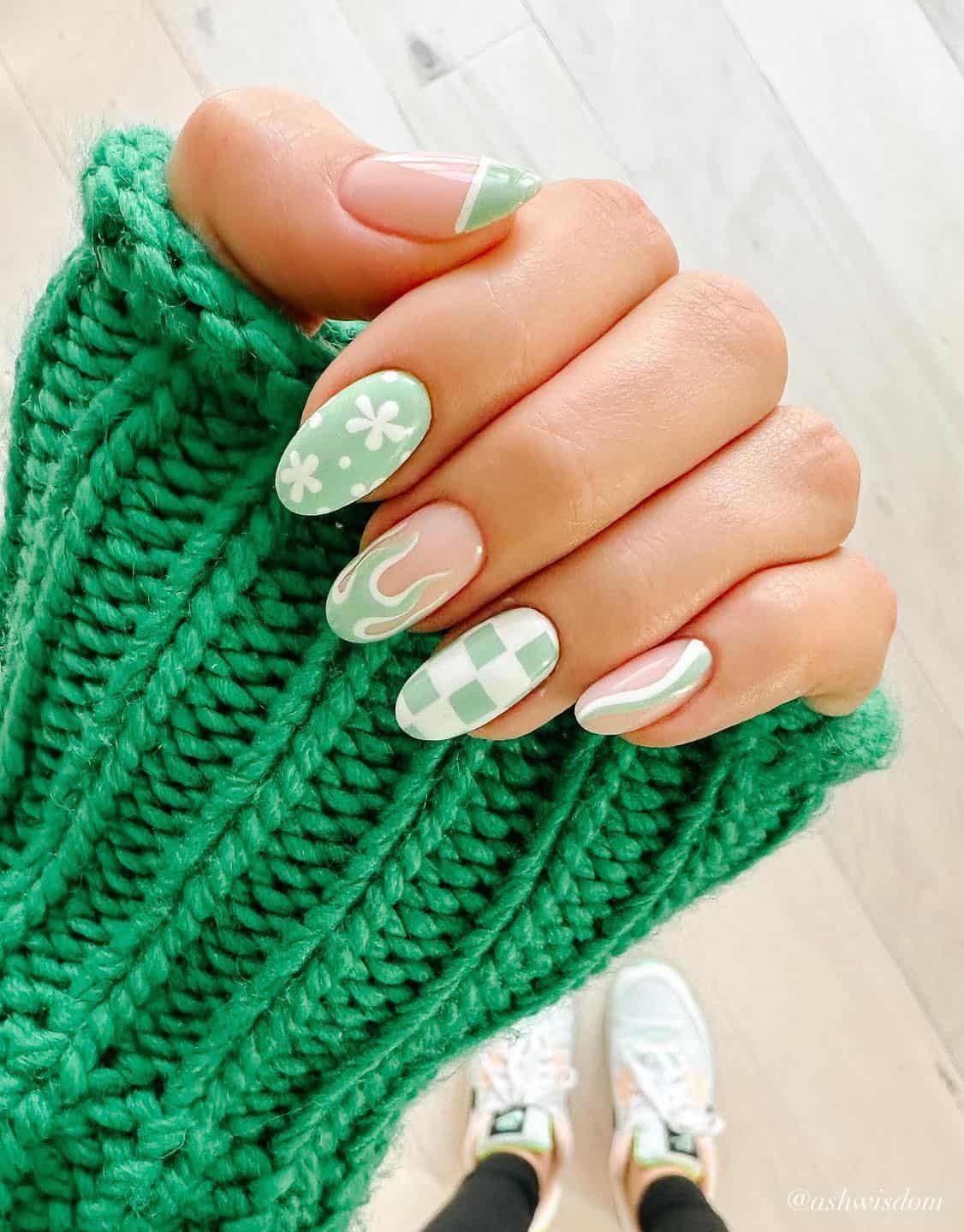 A hand with almond-shaped mint green and white collage nails featuring checkerboard, waves, French tips, flame nail art, and floral patterns