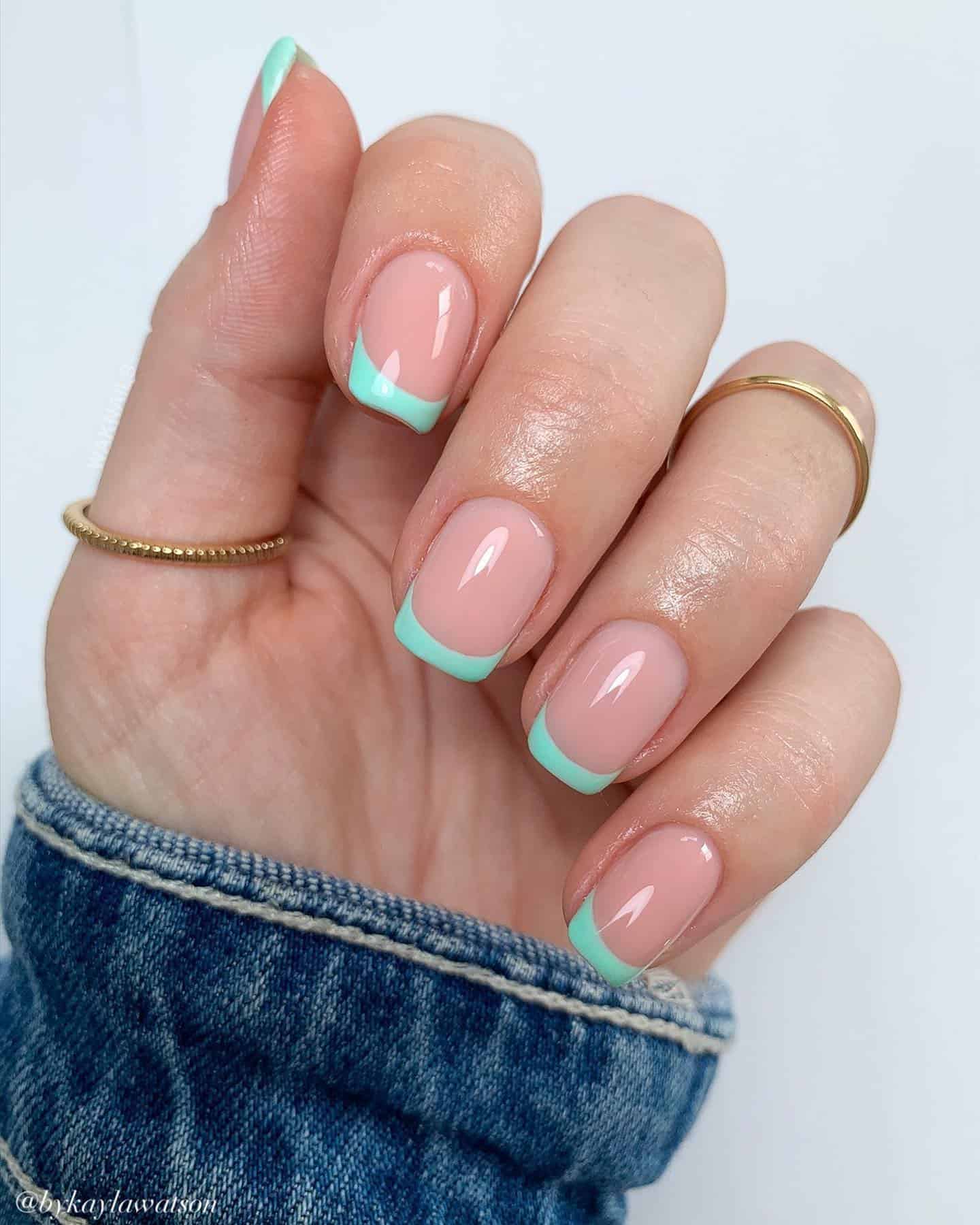 A hand with short square nails painted with mint green French tips