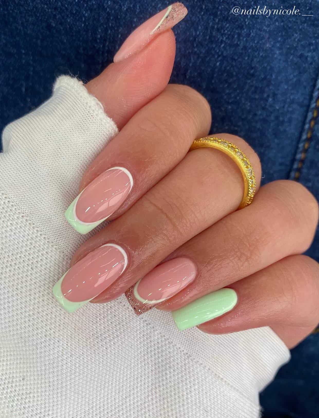 A hand with medium square nails painted a glossy nude with mint green French tips, glitter French tips, white reverse French tips, and a solid mint green accent nail