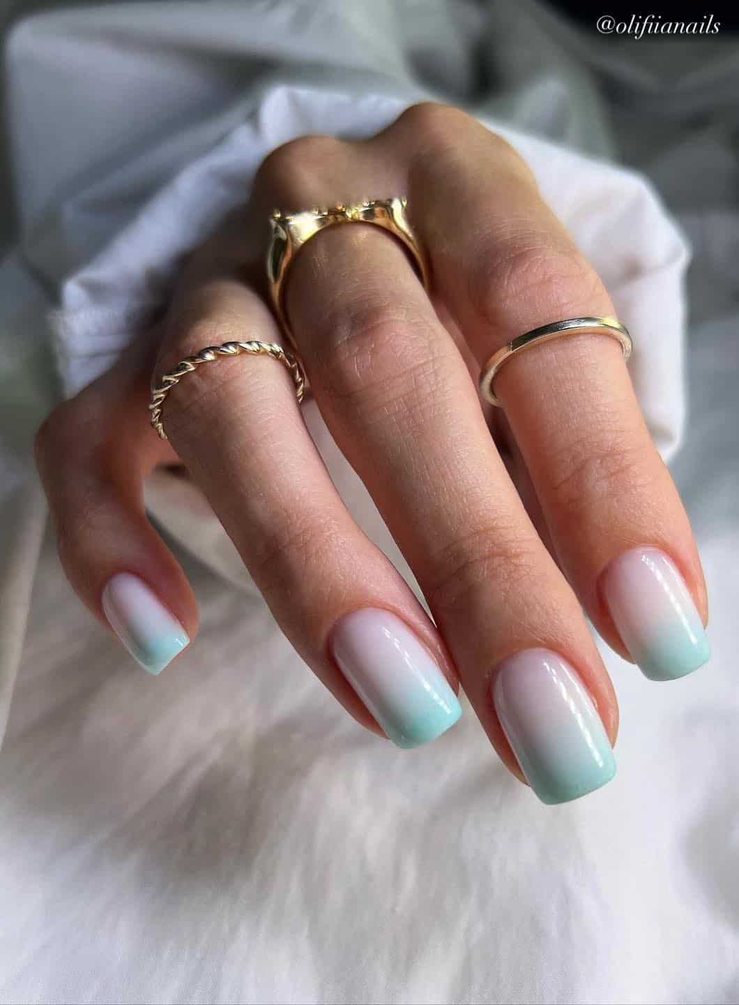 A hand with short square nails painted in a white and mint green ombre