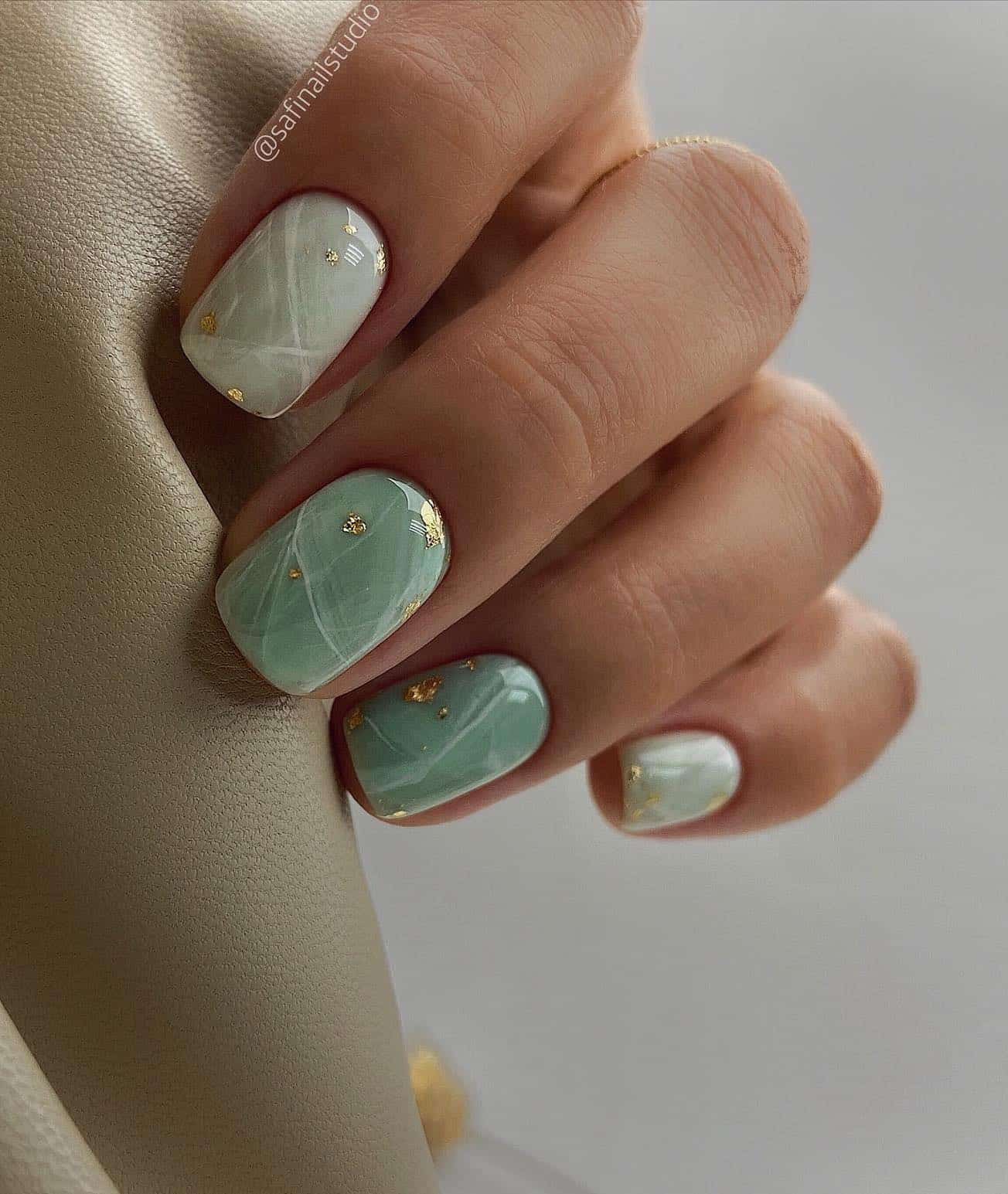 A hand with short marbled mint green nails and gold flake accents