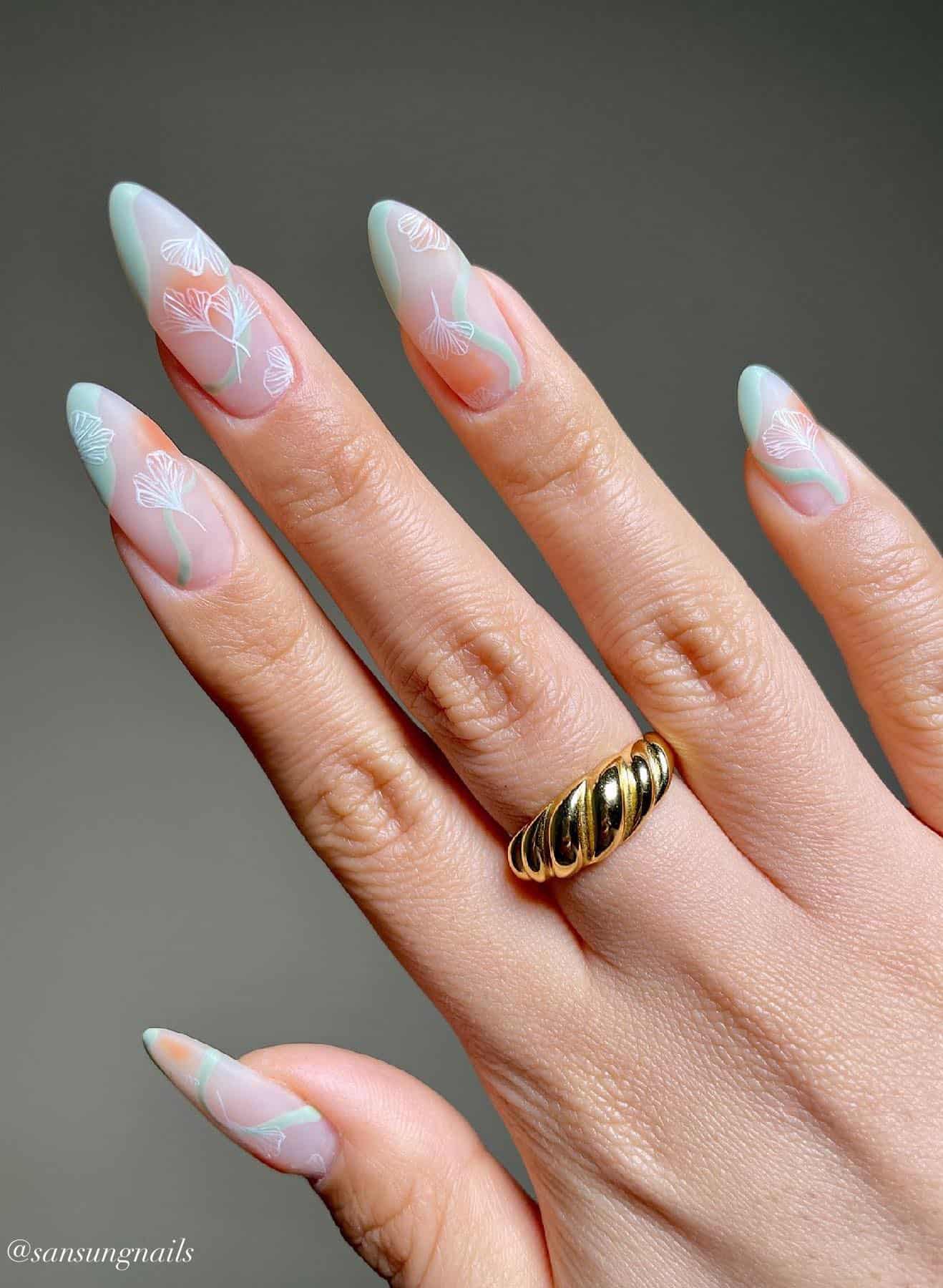 A hand with matte nude nails painted with matte mint green asymmetrical French tips and wave accents with white floral nail art