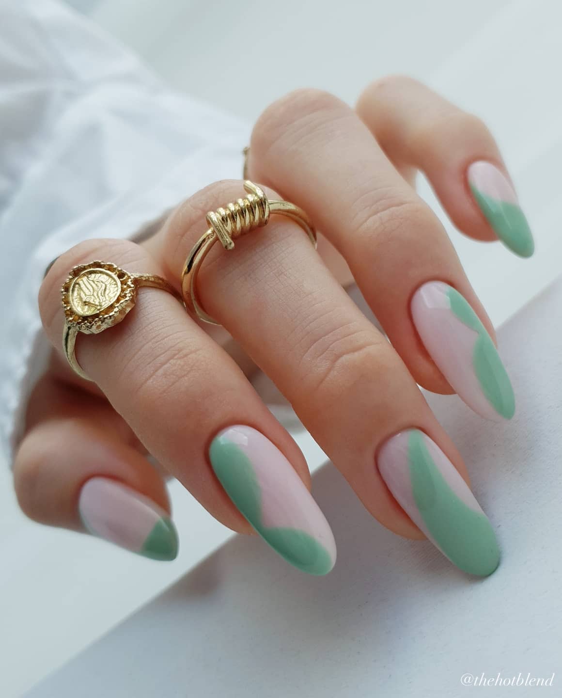 A hand with long almond nails painted a milky white with dark mint green abstract accents