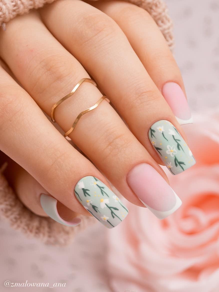 A hand with medium-length square nails painted matte mint green with white flower nail art and two accent nails with classic French tips and a matte finish