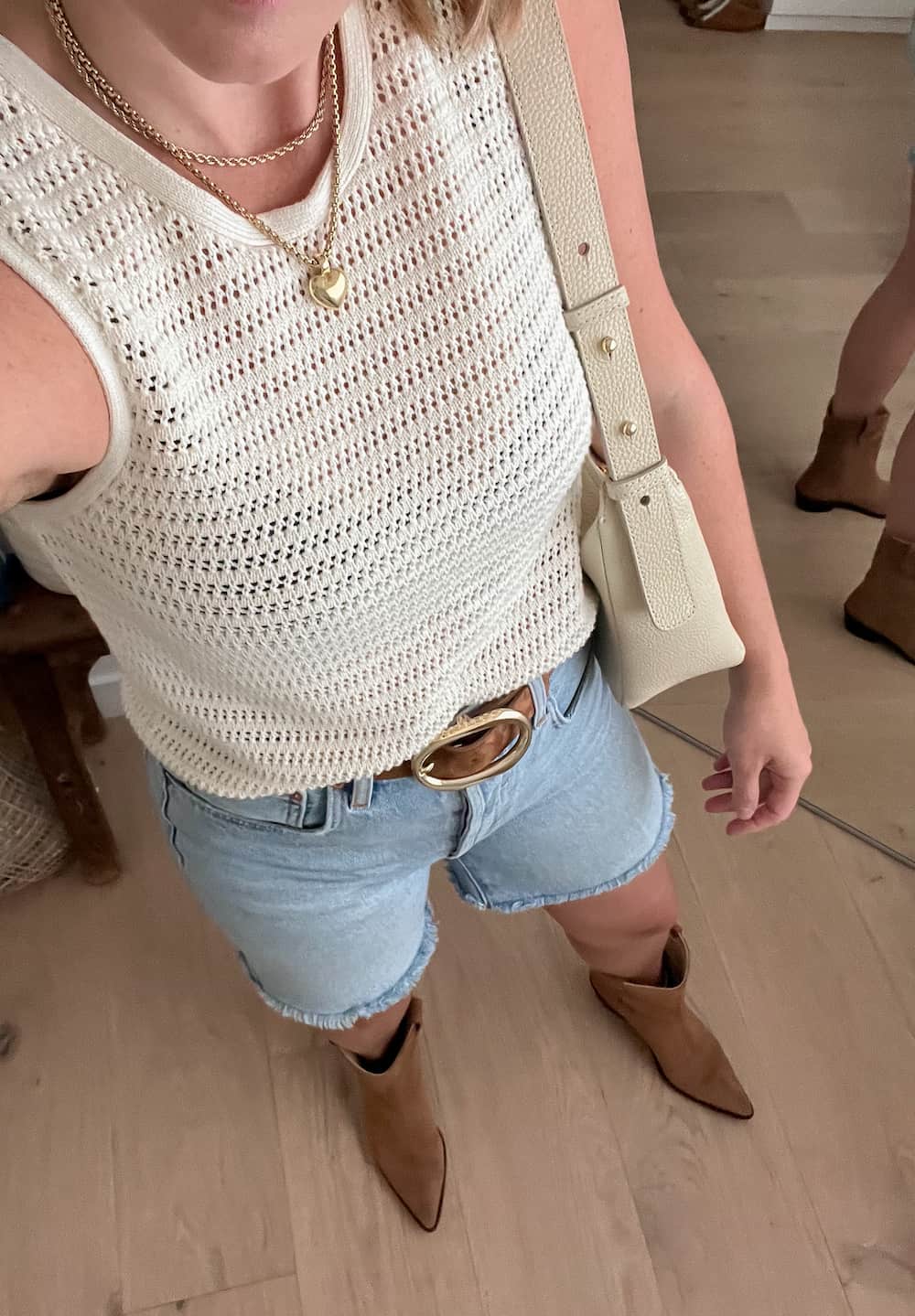 woman wearing a rodeo outfit with a crochet tank top, suede belt with gold buckle, denim shorts, and brown suede western boots