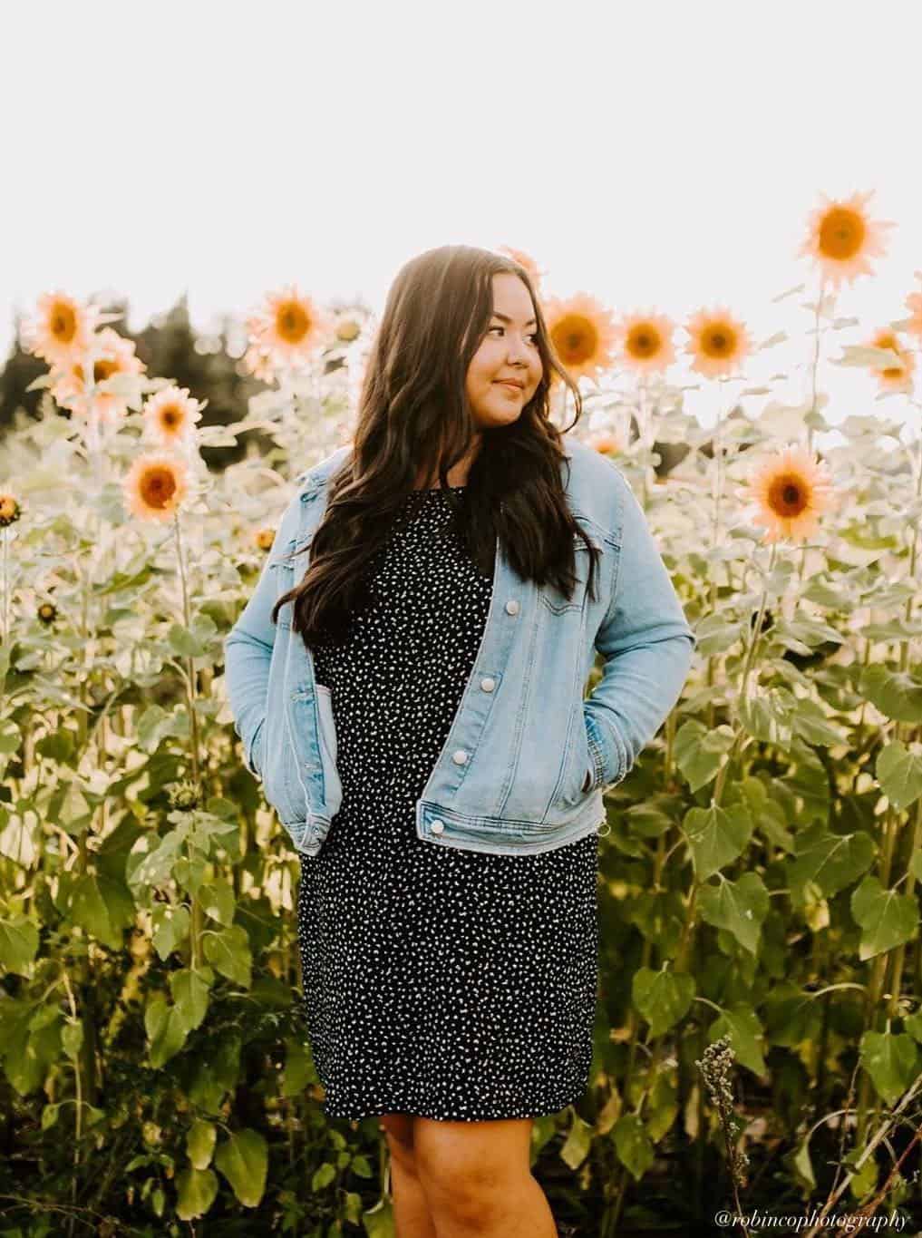 young woman wearing a denim jacket over a black polka dot dress for senior pictures