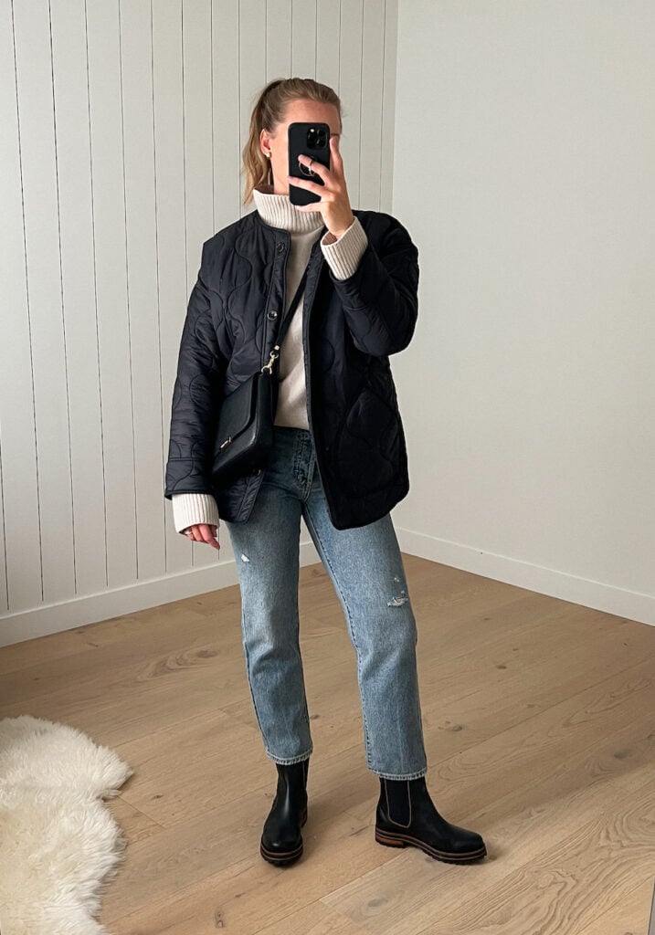 woman wearing a black quilted jacket with straight leg jeans and black chelsea boots