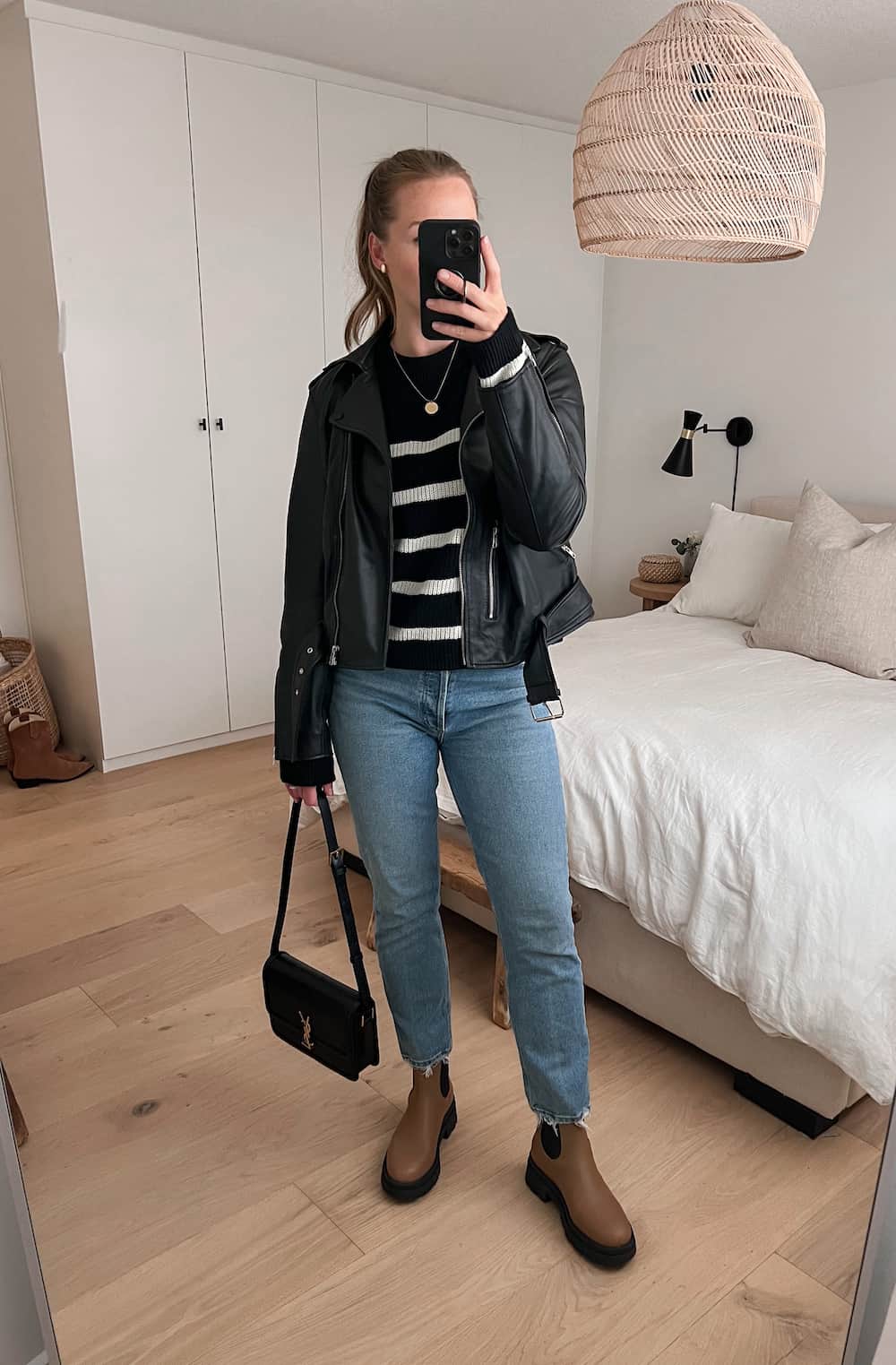woman wearing a black leather jacket over a black striped sweater with blue straight leg jeans and brown Chelsea boots. 