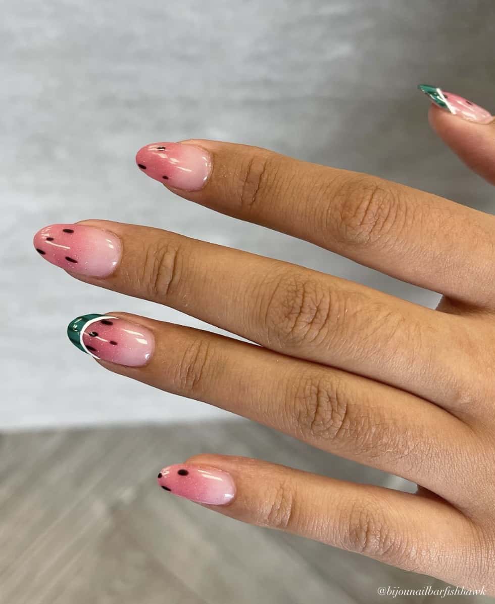 A hand with medium almond nails painted with a pink color with watermelon ombre tips and green rind French tips