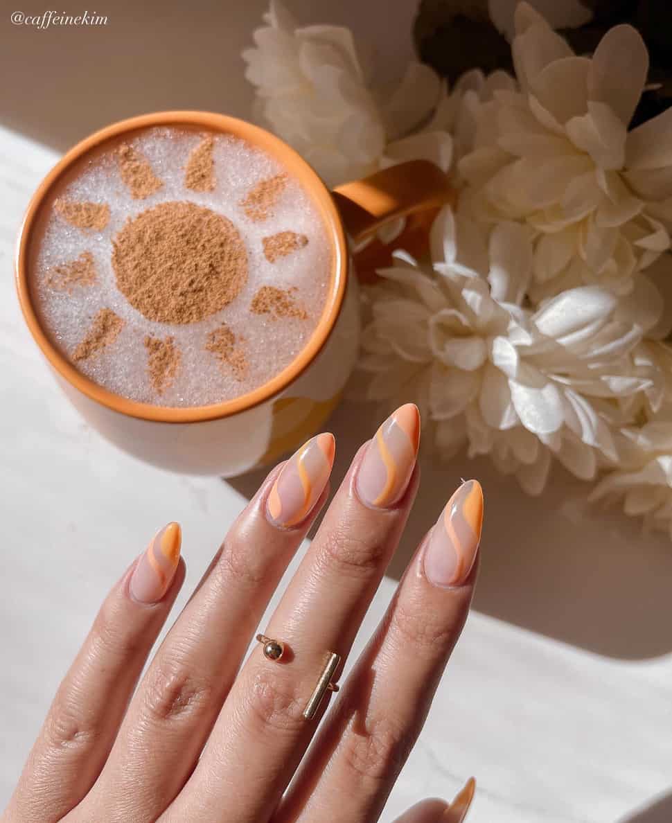 A hand with medium almond nails painted with a nude polish and accented with orange waves