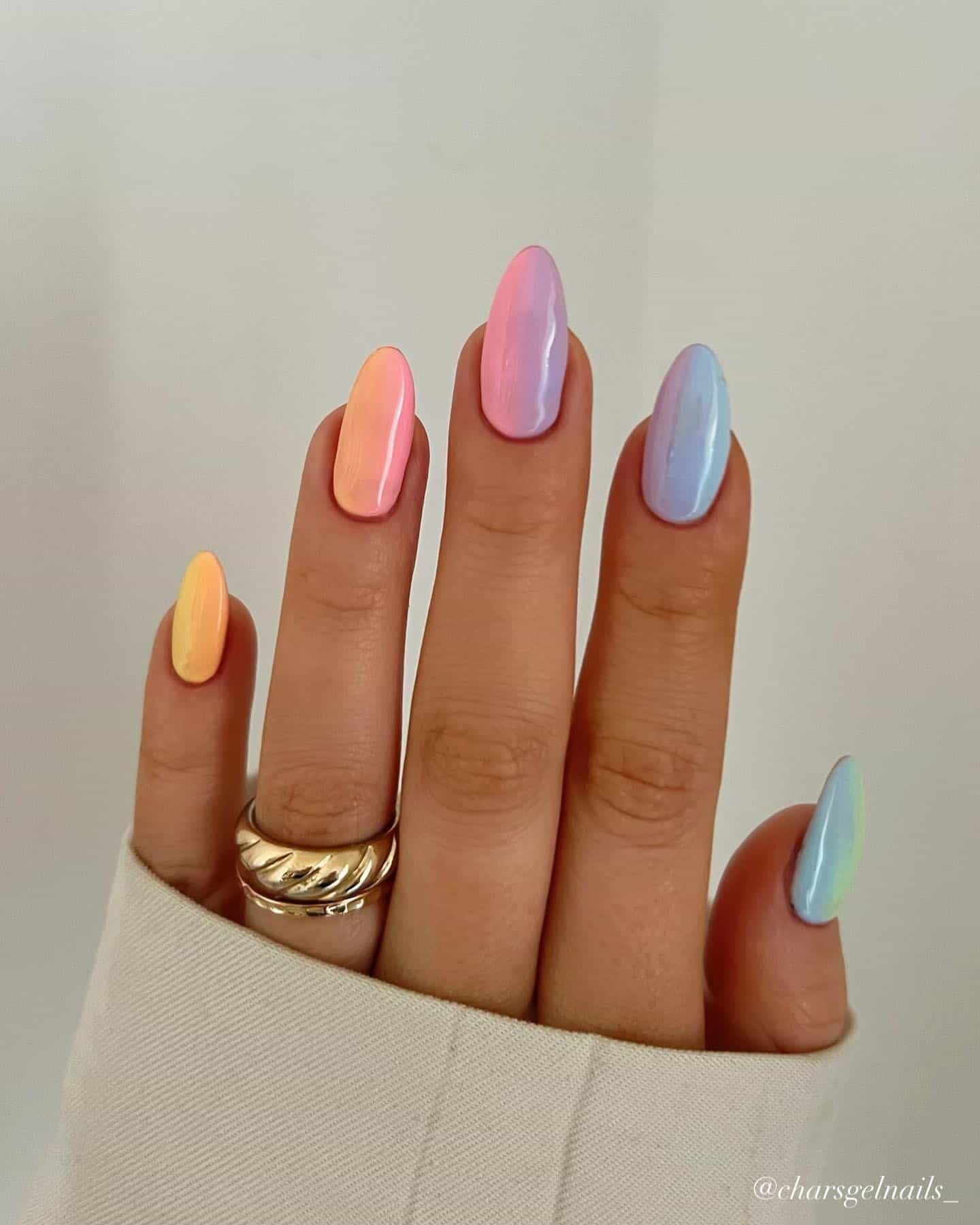 A hand with medium almond nails painted as a rainbow ombre