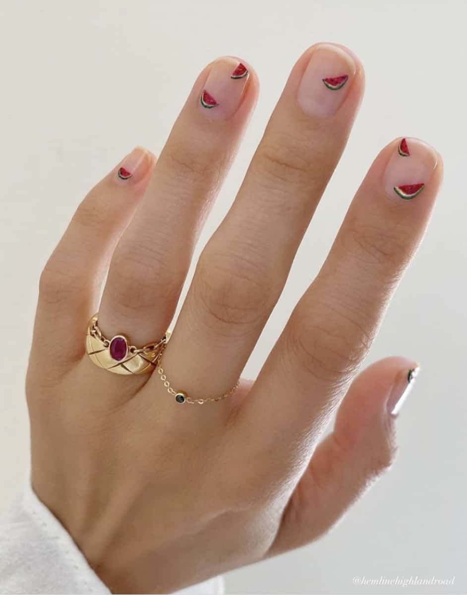 A hand with short nude nails with nail art featuring tiny watermelon slices