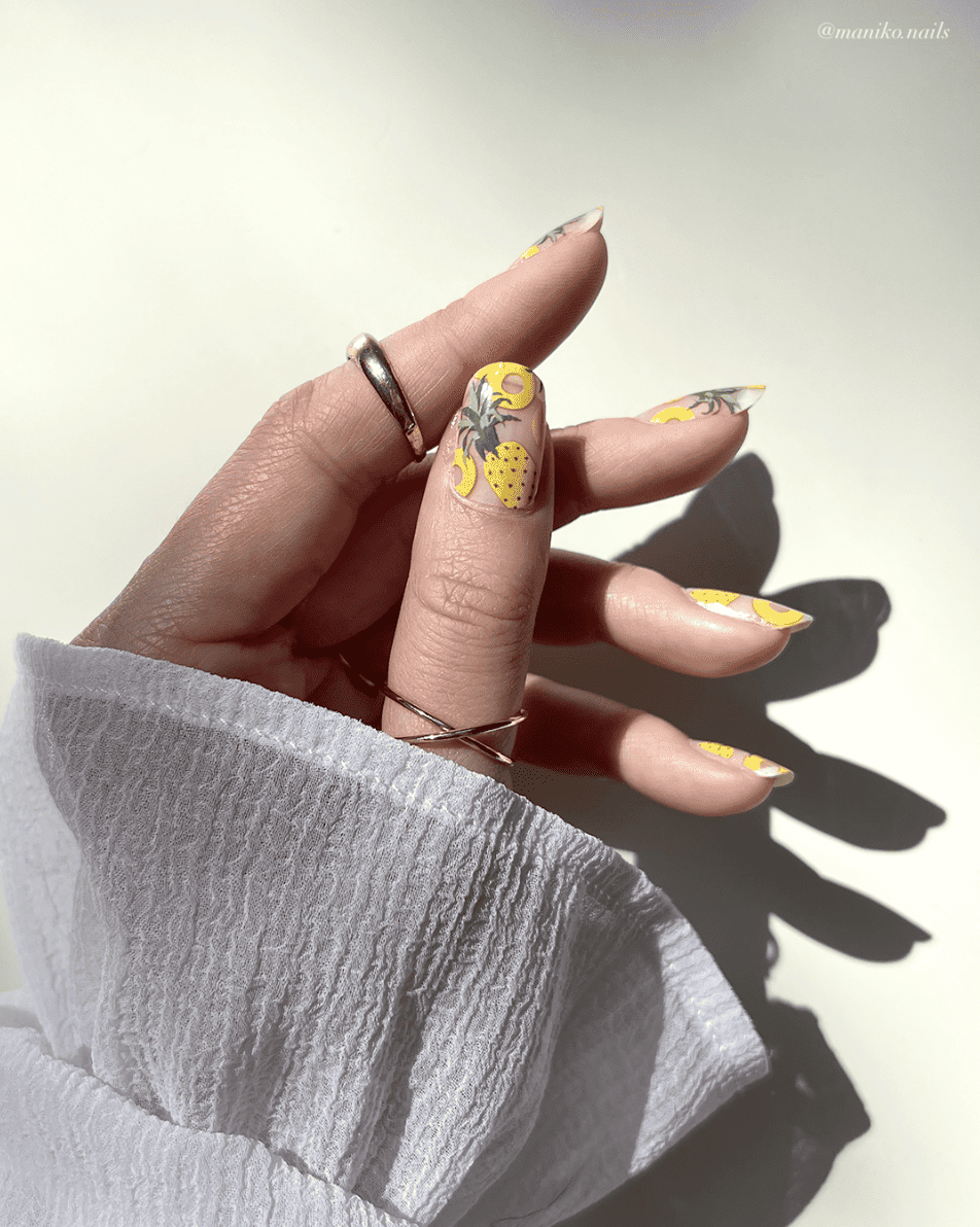 A hand with short squoval nails with a clear coat and painted with pineapple nail art