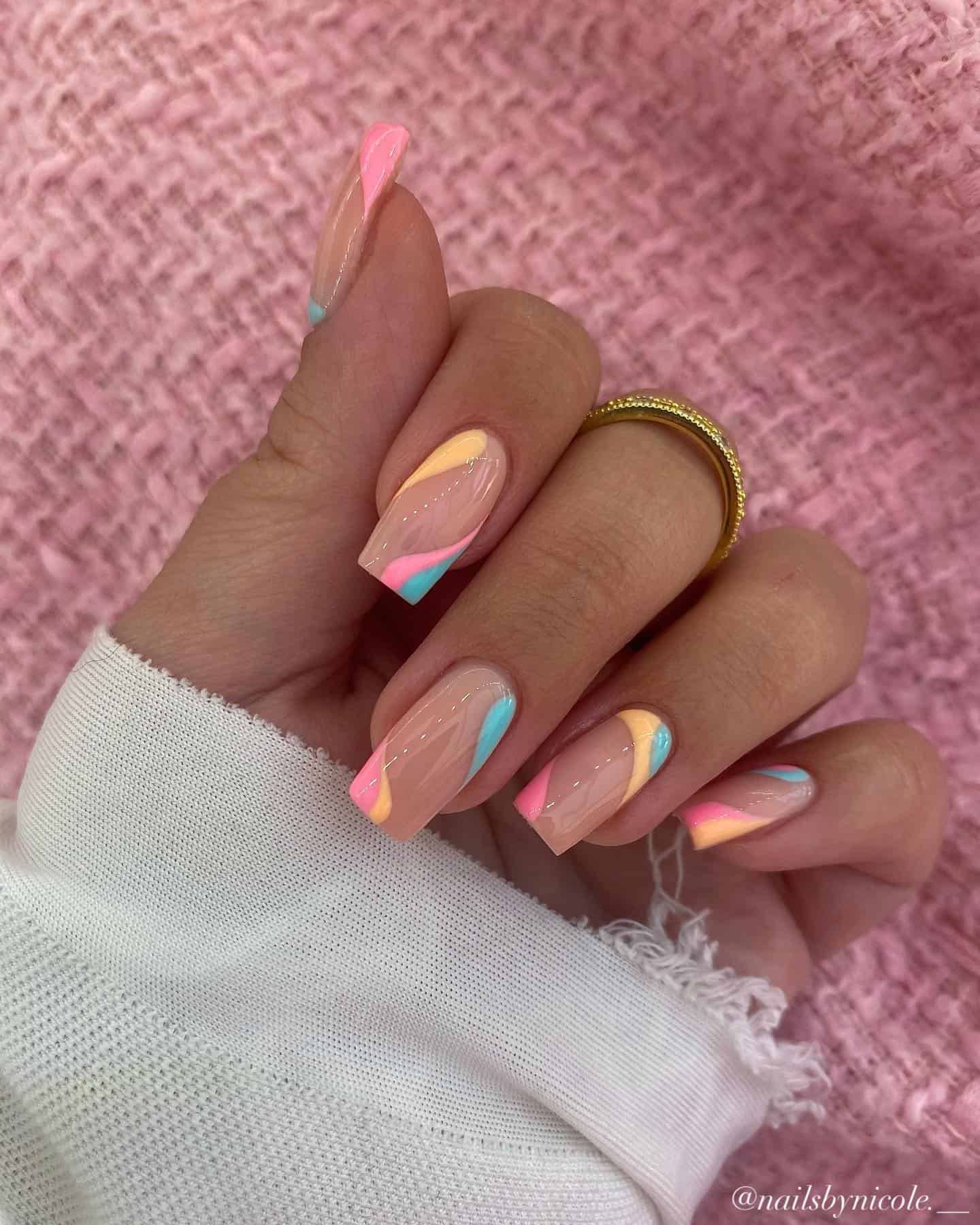 A hand with medium square nails painted a glossy nude color with orange, pink, and light blue wave accents