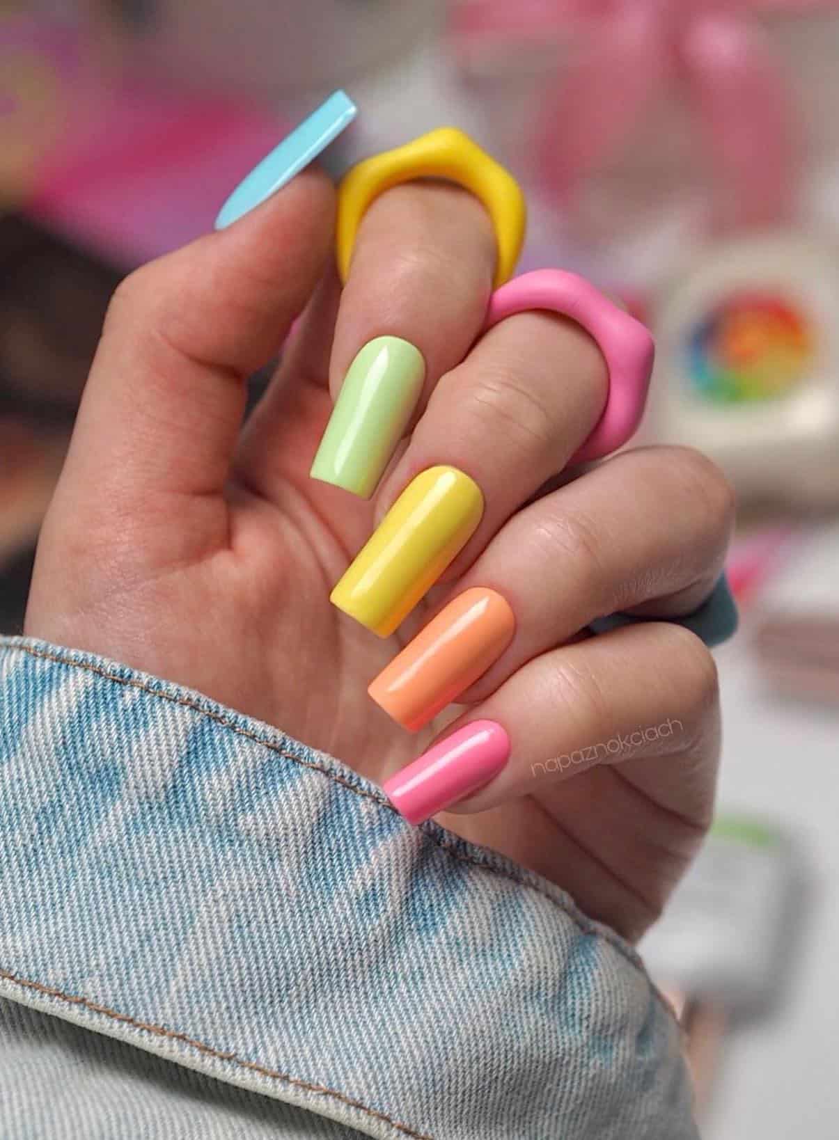A hand with long square nails painted with bright summer colors in a gradient rainbow design