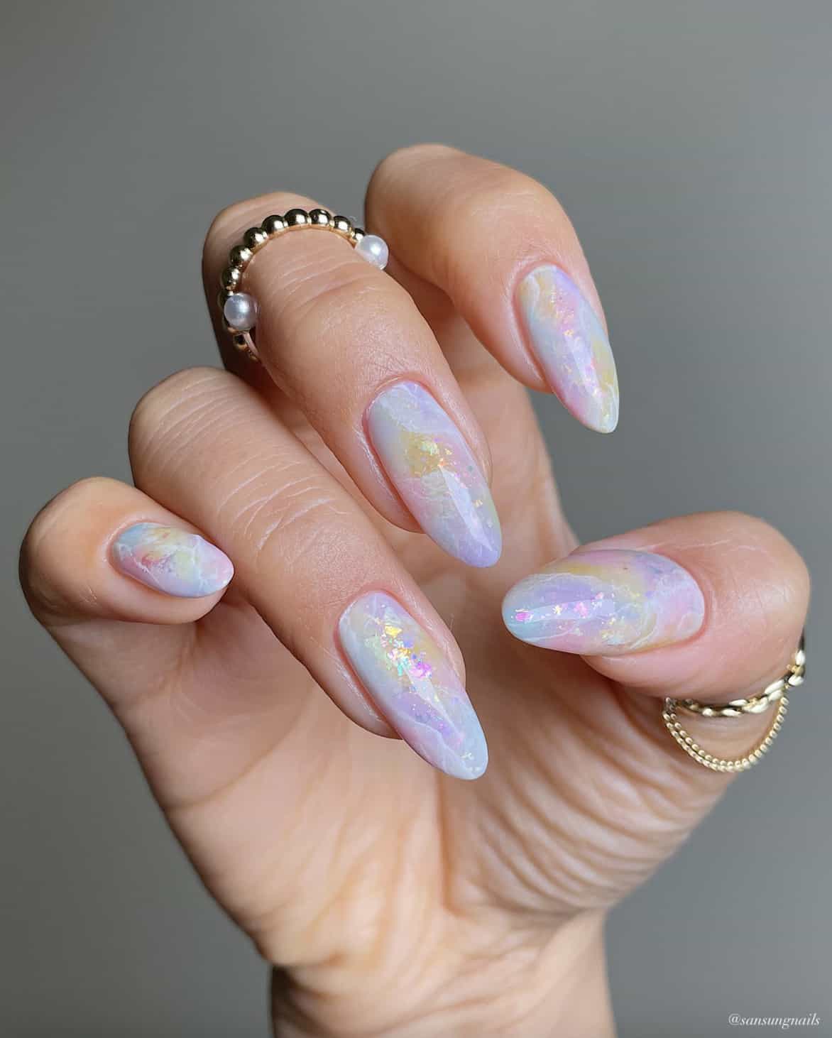 A hand with long almond nails painted with a marbled iridescent design