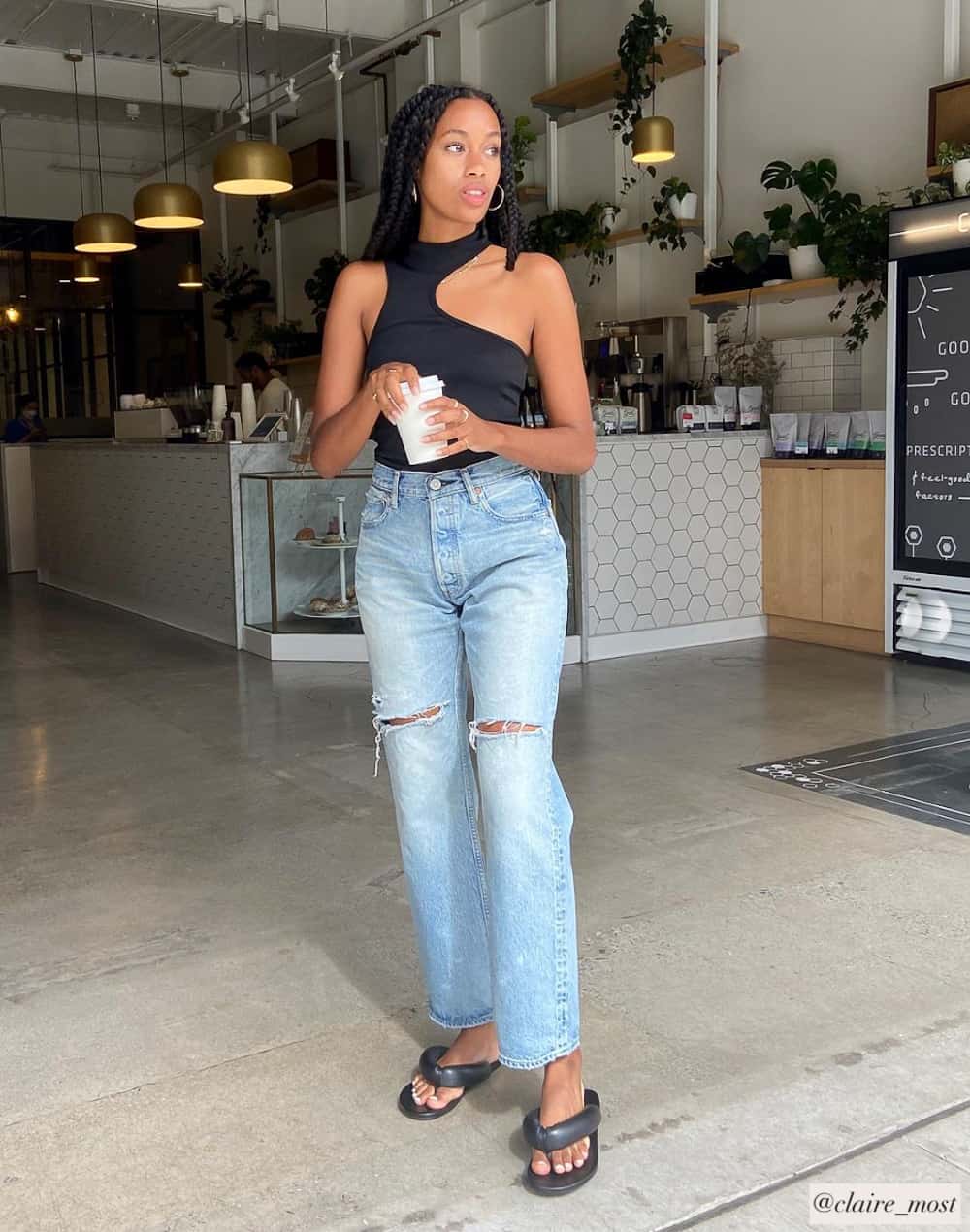 Black woman wearing a stylish outfit with cut out black tank top with straight-leg jeans and puffy flip flop sandals