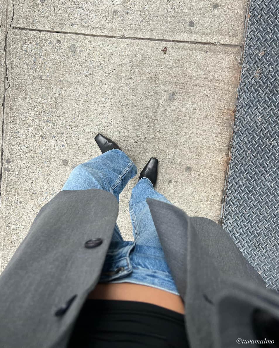 foot selfie view of a woman wearing straight leg jeans with black boots a grey blazer and black crop top