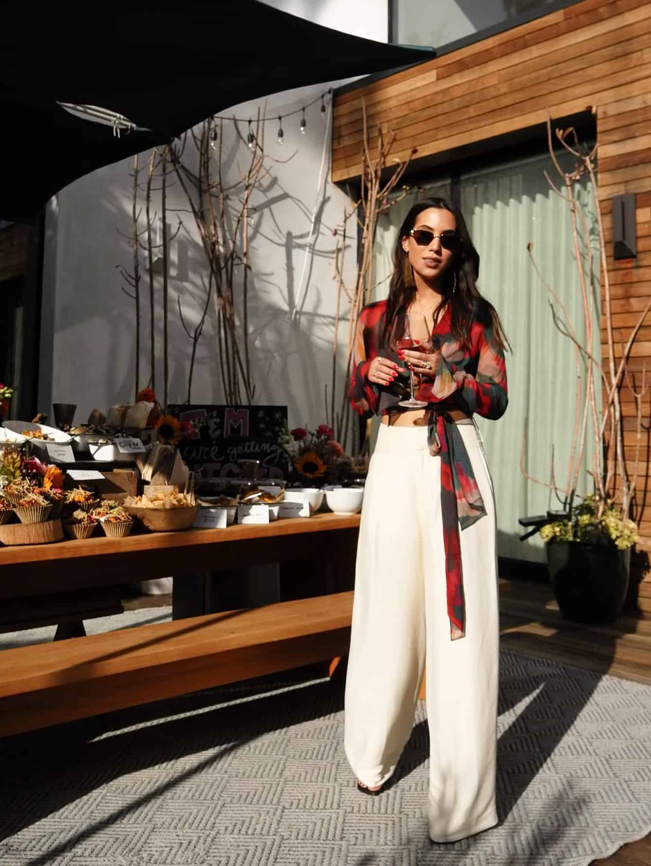 woman wearing a colorful blouse with wide leg palazzo pants holding a glass of wine