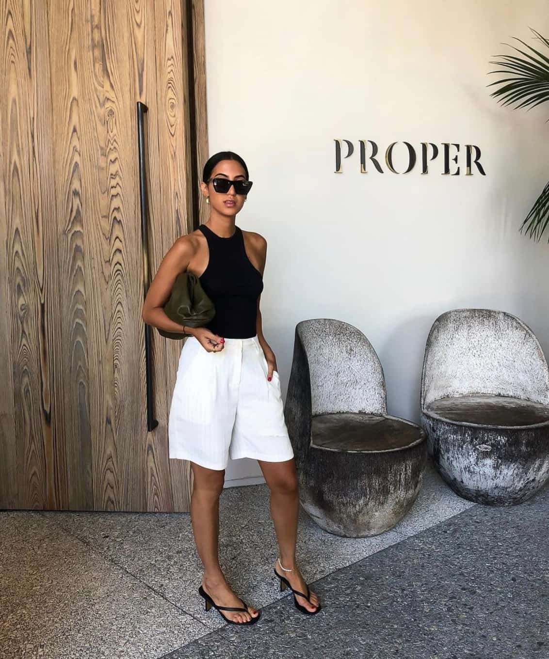 woman wearing a black tank with long white pleated shorts and black kitten heel sandals at a winery