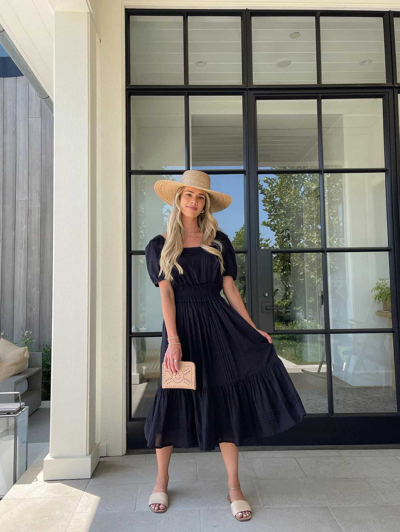 woman wearing a black midi dress with a straw hat and sandals as a chic winery outfit