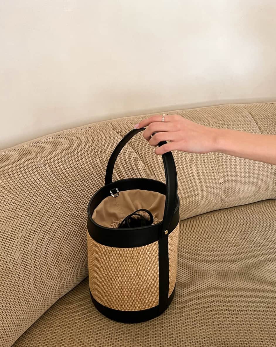 A hand grabbing a raffia and black leather bucket bag from Calvin Klein