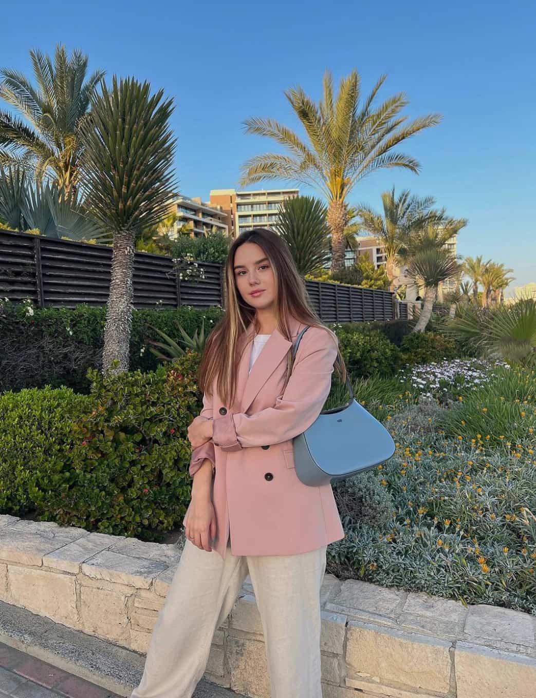 An image of a woman with a blue DKNY purse paired with beige trousers and a pink blazer
