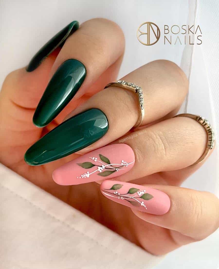 a hand with long almond nails painted solid forest green and matte pink accent nails with leaf and white floral nail art