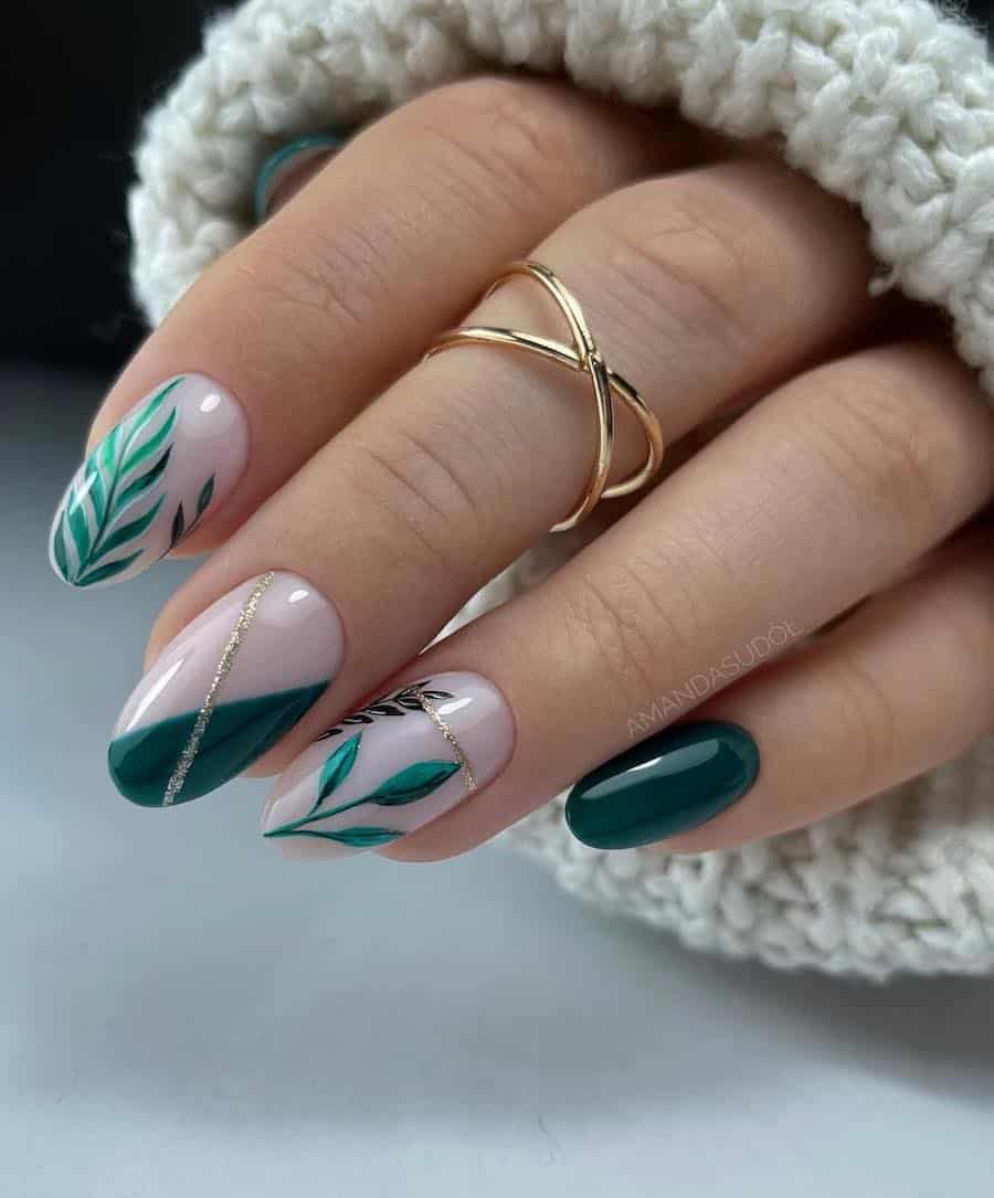 a hand with short round nails painted in milky white and forest green shades with leaf nail art and gold glitter details