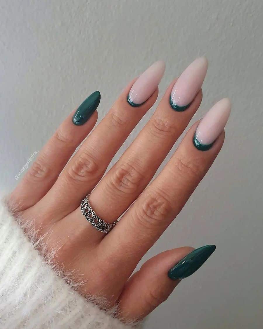 a hand with long almond nails painted in solid-colored dark green and three milky white nails with forest green reverse French tips
