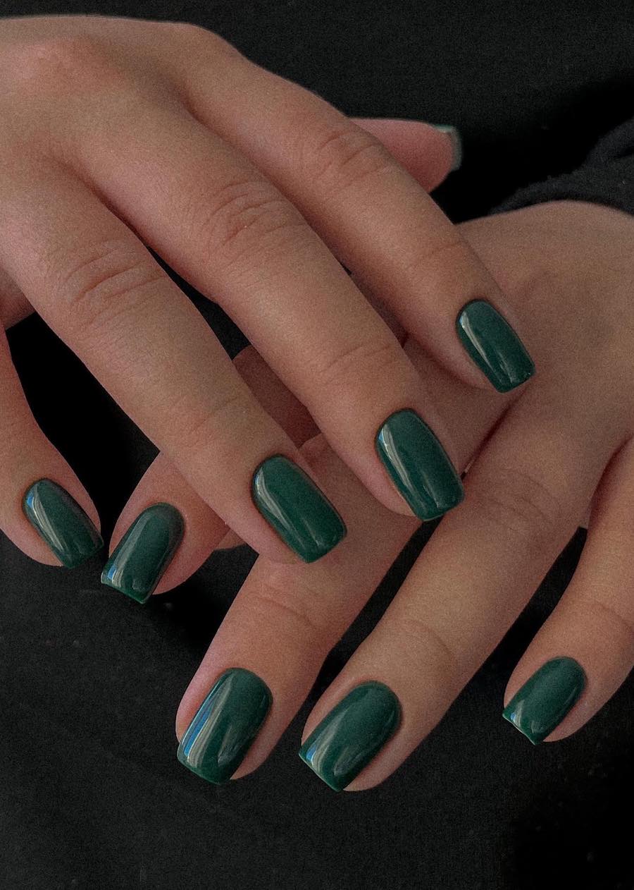 a hand with short square nails painted a solid-colored forest green