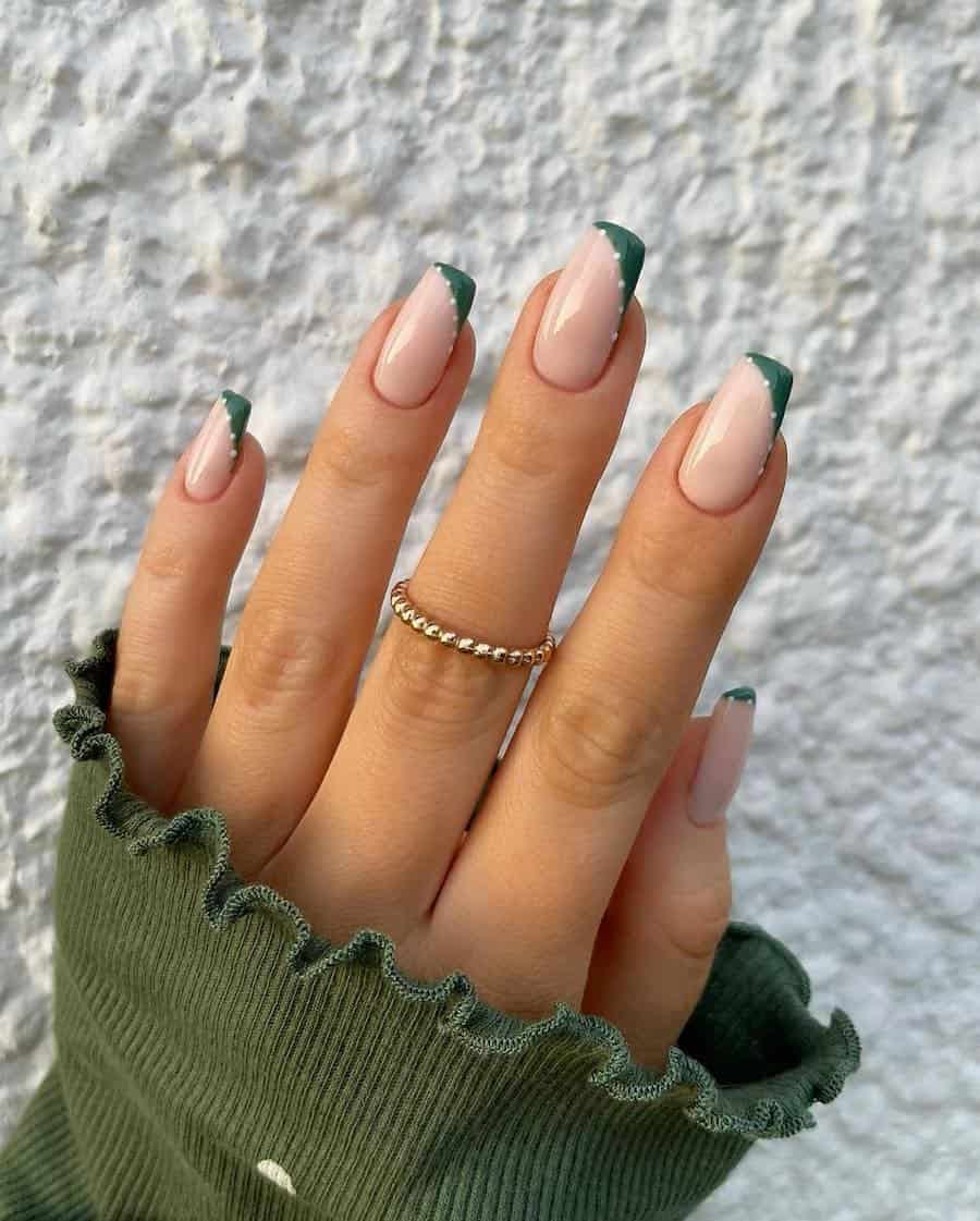 a hand with pinkish-white square nails with asymmetrical forest green French tips with white dot accents
