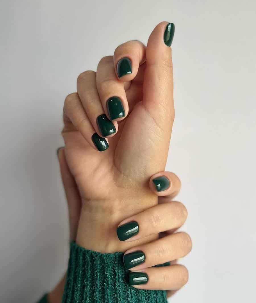 a hand with short solid-colored dark green nails with a glossy finish