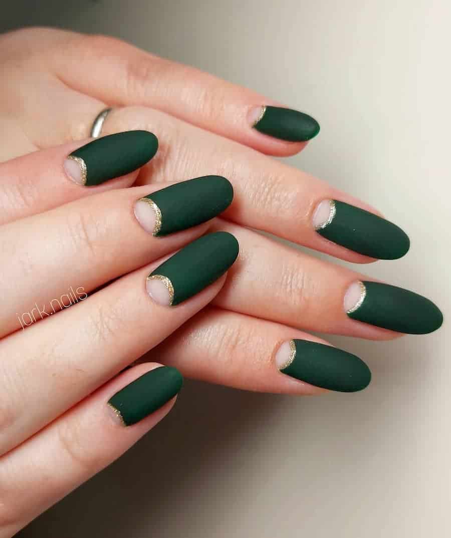 a hand with long round nails with matte dark green and nude half moons with gold glitter borders