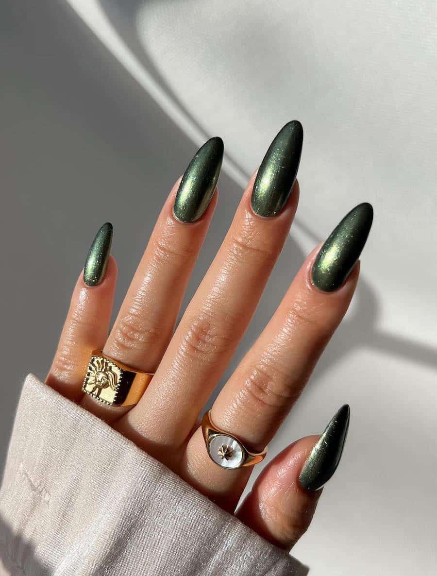 a hand with long almond nails painted in a dark green nail polish with a chrome finish