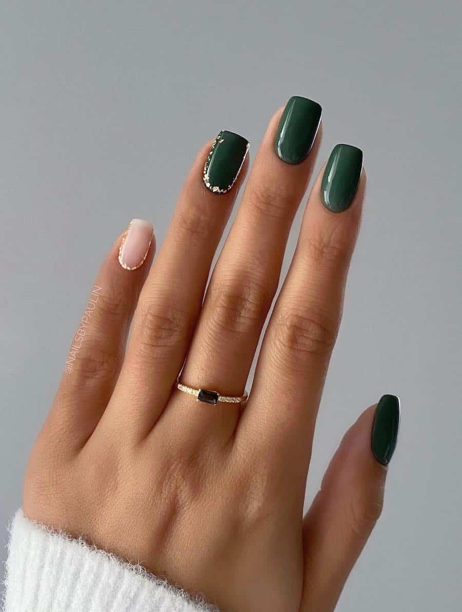a hand with short squoval nails painted in a forest green color with one nude accent nail and silver flakes details