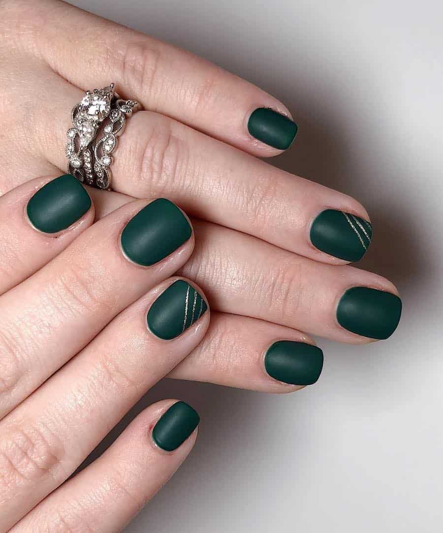 a hand with short dark green nails with a matte finish and gold accent lines on one finger