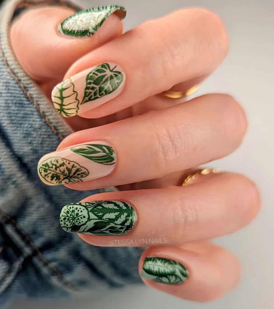 a hand with medium-length squoval nails painted light green with two nude nails all painted with forest green tropical leaf nail art