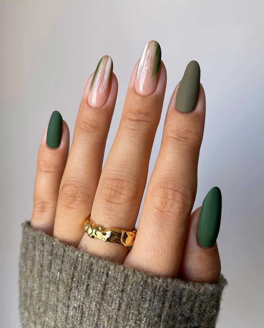 a hand with long almond nails painted in a combination of glossy nude, matte olive green, and matte forest green polish with white and glitter accents