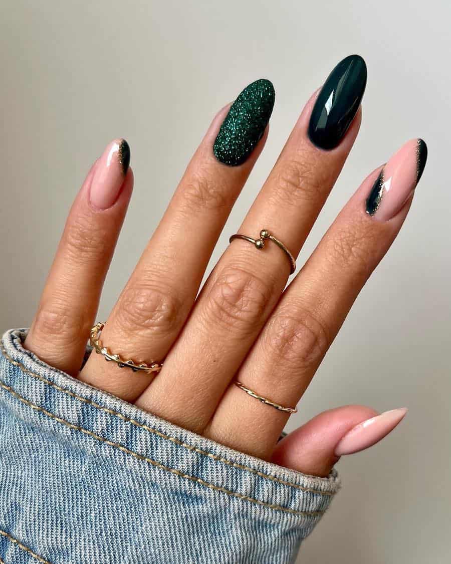 a hand with medium-length almond nails painted nude and glossy dark green with sparkly forest green and gold glitter accents