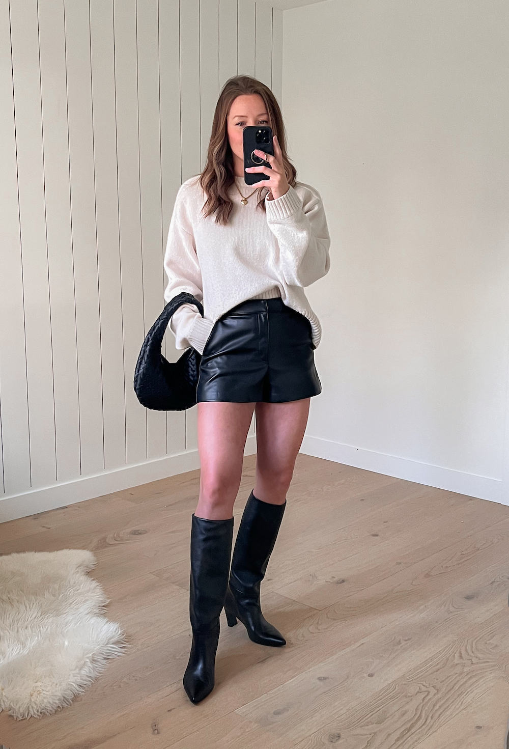 woman wearing a chunky ivory knit sweater with black leather shorts and black knee-high boots