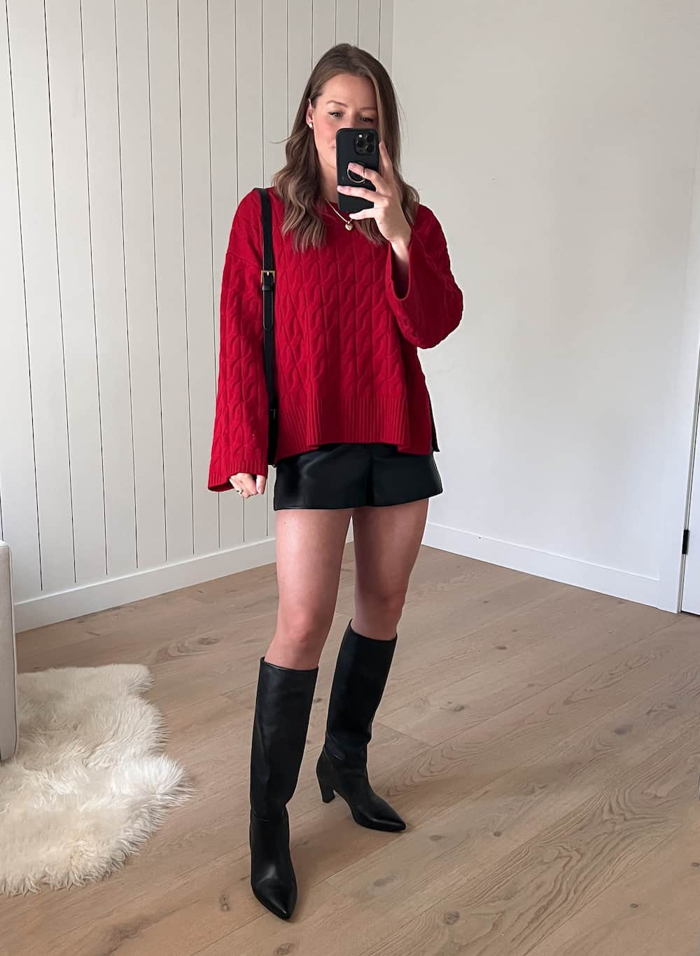 woman wearing a chunky red cable knit sweater with black leather shorts and black knee-high boots