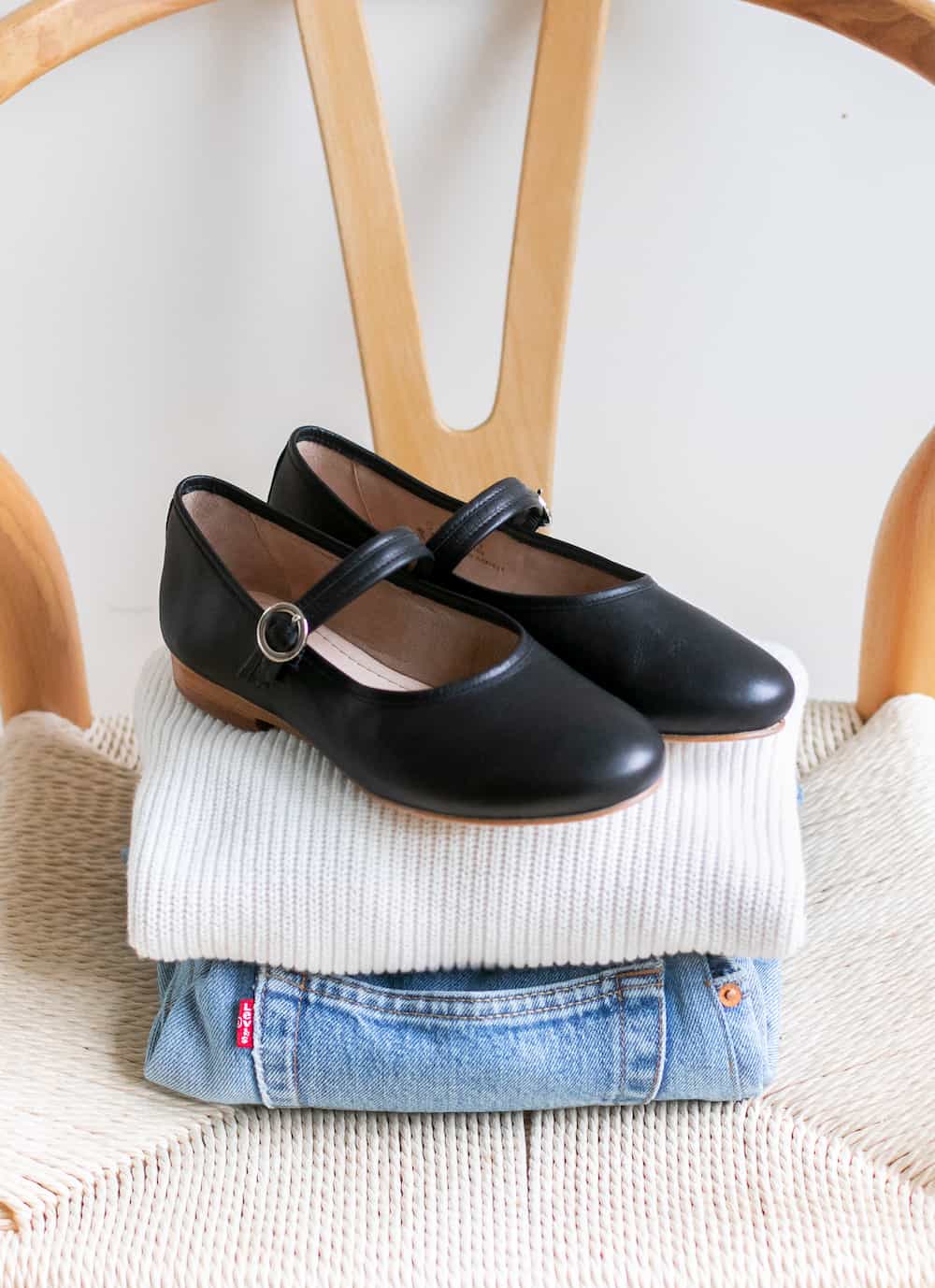 a pair of black Poppy Barley Mary Jane shoes sitting on a chair on top of a folded ivory sweater and pair of blue jeans