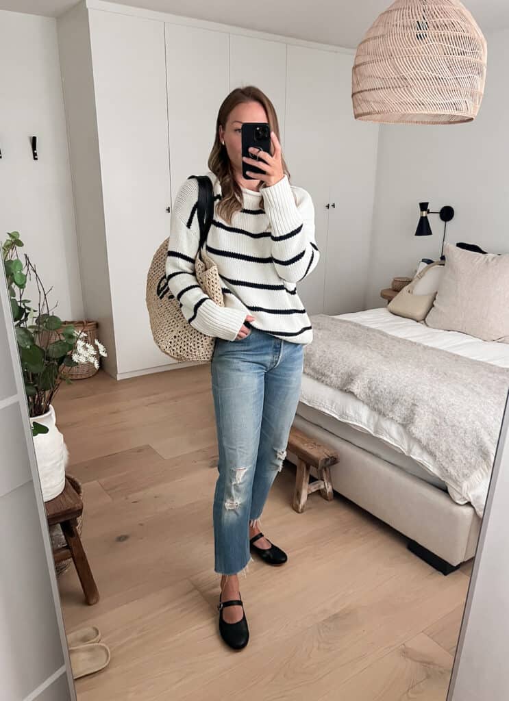 woman wearing a striped knit sweater with blue jeans and black Poppy Barley Mary Jane flats with a raffia Anine Bing tote bag