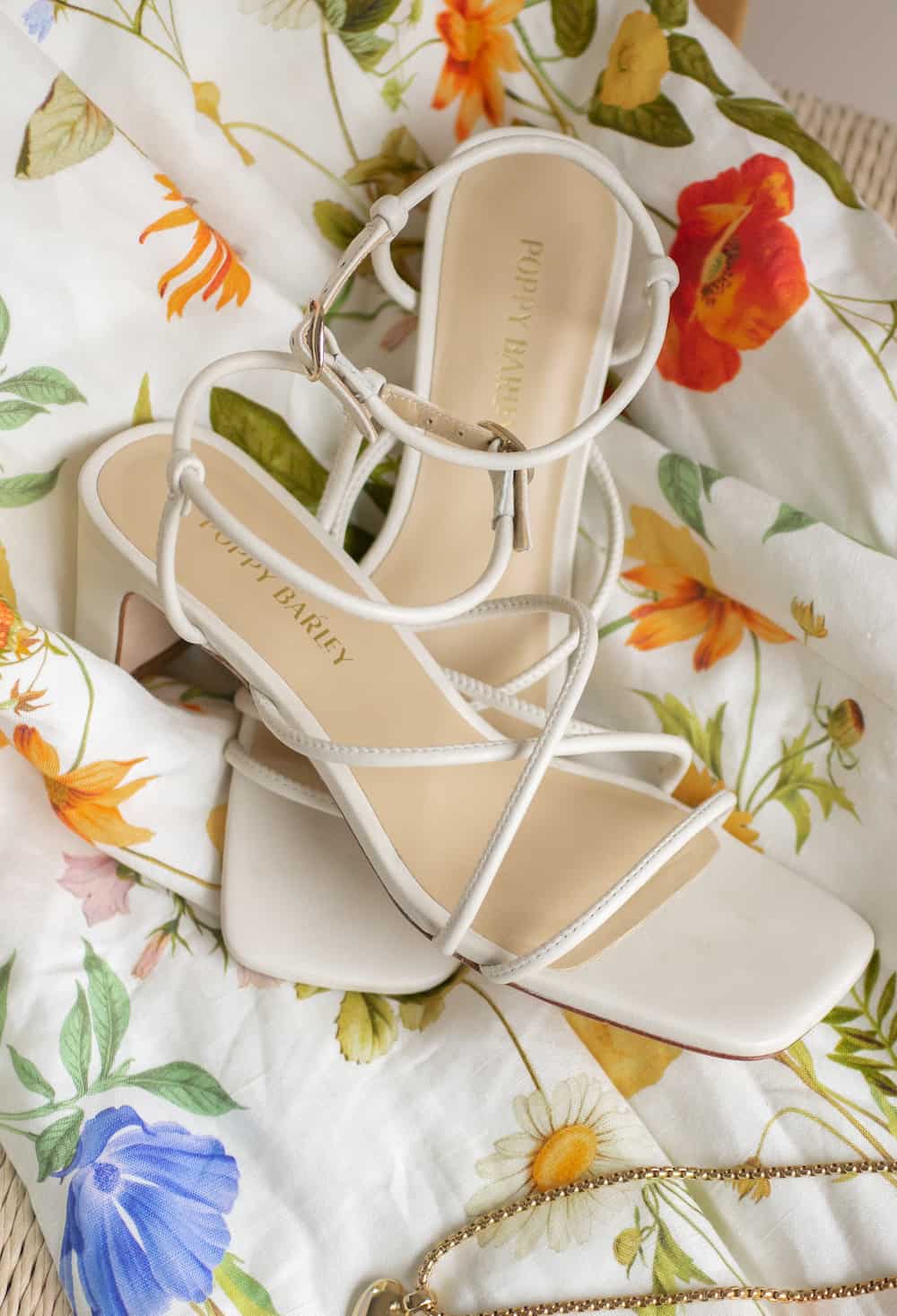 a pair of ivory heeled Poppy Barley sandals on top of a floral dress